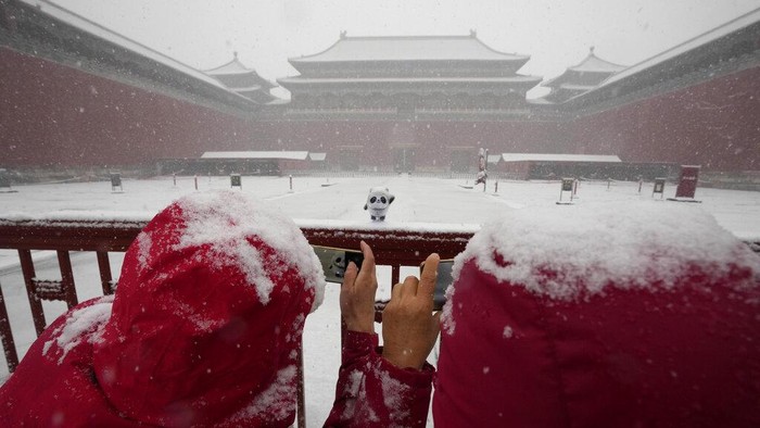 A figurine of Bing Dwen Dwen, the 2022 Winter Olympics mascot is placed on a gate by visitors to the Forbidden City as it snows on Friday, March 18, 2022, in Beijing. (AP Photo/Ng Han Guan)