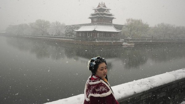 Seorang wanita mengenakan kostum periode tradisional berfoto di dekat Kota Terlarang saat salju turun di Beijing, China, Jumat (18/3/2022) waktu setempat.  