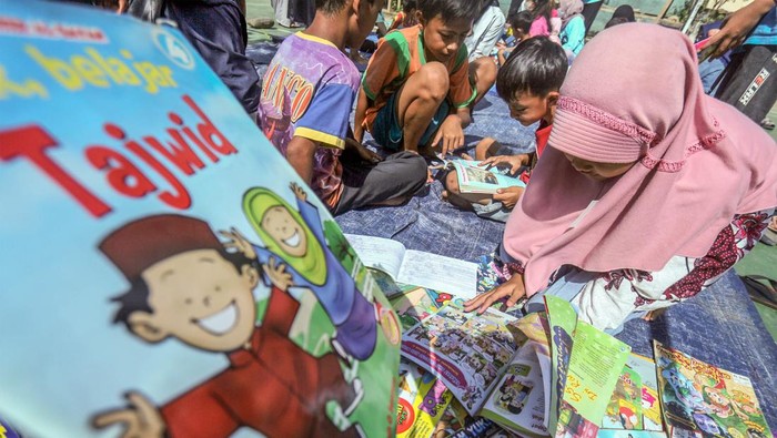 Inspiratif! Perpustakaan Keliling demi Tingkatkan Minat Baca Dua anak membaca buku yang dipinjam dari perpustakaan keliling di Pabuaran, Cibinong, Kabupaten Bogor, Jawa Barat, Minggu (20/3/2022). Perpustakaan keliling yang digelar oleh komunitas Cibinong Society itersebut untuk menambah ilmu pengetahuan serta meningkatkan minat baca terhadap anak di usia dini di kawasan perkampungan. ANTARA FOTO/Yulius Satria Wijaya/YU