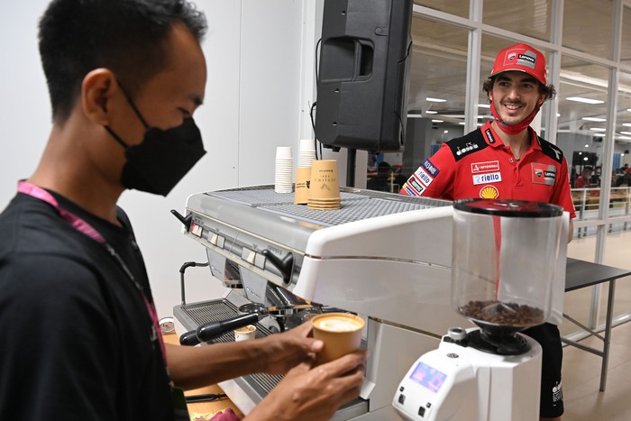 Pembalap Ducati Lenovo Team Francesco Bagnaia (kanan) menerima kopi pesanannya dari barista Sedjiwa Kopi di media center usai balapan MotoGP seri Pertamina Grand Prix of Indonesia di Pertamina Mandalika International Street Circuit, Lombok Tengah, NTB, Minggu (20/3/2022) malam. Stan kopi tersebut memberikan layanan kopi gratis bagi para pembalap dunia, kru tim balap serta media dari berbagai negara yang meliput acara MotoGP Mandalika sebagai sarana promosi kopi Indonesia terutama kopi lokal Lombok ke kancah internasional. ANTARA FOTO/Andika Wahyu/nym.