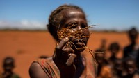 Seorang wanita memegang bagian dari tanaman jagung yang mati di ladang yang tertutup pasir merah, di Anjeky Beanatara, wilayah Androy, Madagaskar.