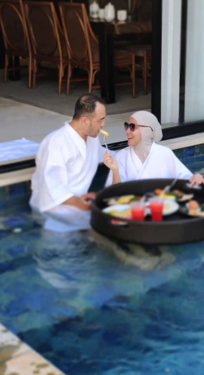 Seperti inilah potret bulan madu keduanya. Berada di kolam berenang saat berada di villa di Bali, Venna Melinda menyuapi suaminya. Foto: Instagram