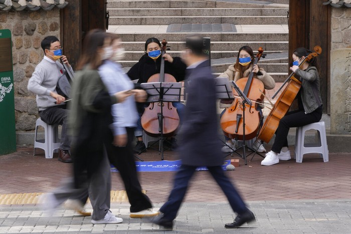 A professor and students from Ewha Womans University wearing masks in the colors of Ukraine's flag hold an outdoor mini-concert for peace in Seoul, South Korea, Monday, March 21, 2022. (AP Photo/Lee Jin-man)
