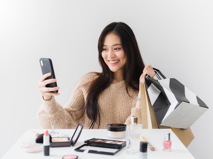 Ilustrasi wanita belanja kosmetik Asian beautiful women blogger are using the smartphone live streaming online with a shopping bag In the white room with cosmetics on table.Concept of online shopping business.