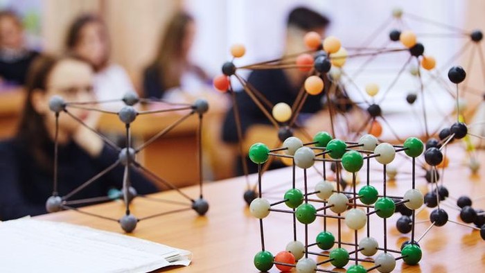 Students sit in the classroom and listen to a lecture in science. Plastic molecular educational model. Soft focus background image.