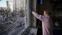 Seorang wanita mengukur jendela sebelum menutupinya dengan lembaran plastik di sebuah gedung yang rusak akibat bom di Kyiv, Ukraina, Senin (21/3/2022) waktu setempat. (AP/Vadim Ghirda)  