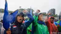Massa buruh tampak memakai jas hujan di lokasi demo.