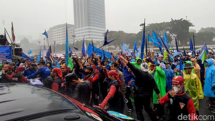 Massa buruh menggelar aksi unjuk rasa di depan Gedung DPR RI, Jakarta. Meski diguyur hujan deras, mereka tetap beraksi menuntut UU Cipta Kerja dicabut.