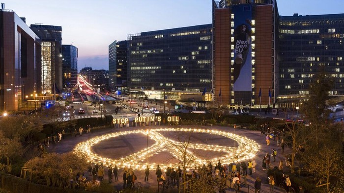 People stand around a giant peace sign with the message 'Stop Putin's Oil', put up by demonstrators ahead of an EU and NATO summit in Brussels, Tuesday, March 22, 2022. Protestors on Tuesday called on EU leaders to impose a full ban on Russian fuels and to hold one minute of silence to honor the victims of war. (AP Photo/Geert Vanden Wijngaert)