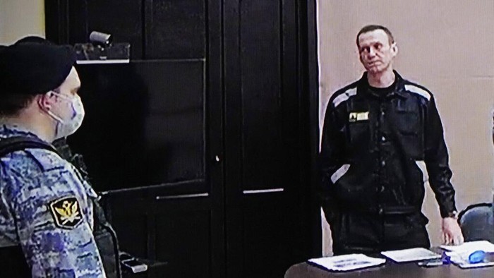 Russian opposition leader Alexei Navalny, centre, gestures via a video link provided by the Russian Federal Penitentiary Service, standing next to his layer and speaking with Penitentiary Service officers during a court session, in Pokrov, Vladimir region, about 100 kilometers (62 miles) east of Moscow, Russia, Tuesday, March 22, 2022.  Navalny has been convicted of fraud and contempt of court and sentenced to nine years in a maximum security prison. A judge also ruled Tuesday that Navalny would have to pay a fine of 1.2 million rubles (about $11,500).  (AP Photo/Alexander Zemlianichenko)