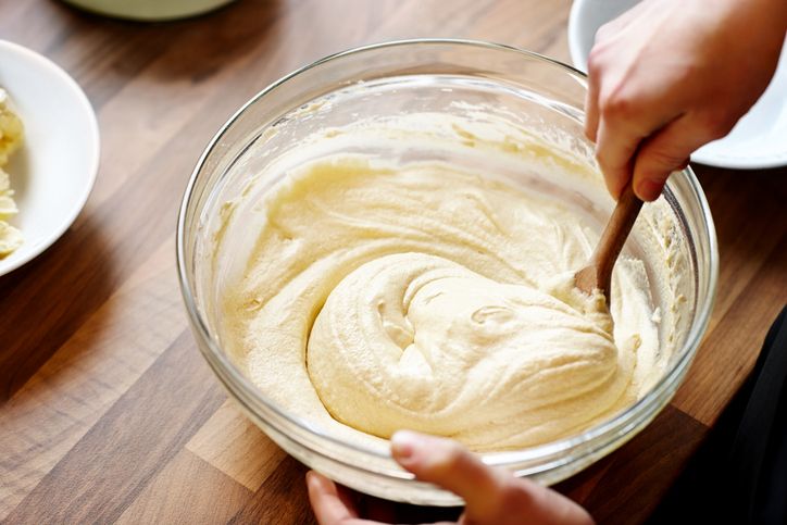 Hands of young female chopping fresh onion on wooden board while preparing italian pasta with vegetables and minced meat