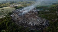 Sedikitnya 120 ton sampah dibuang di sana. Tampak asap di antara gunungan sampah. 