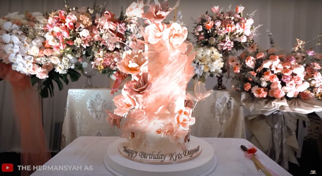 Sesuai dengan tema dekorasi ulang tahun Krisdayanti, kue ulang tahunnya pun dibuat dengan warna yang senada. Kue tersebut terlihat begitu cantik dengan hiasan bunga-bunga berwarna salem. Pada bagian bawah kue terdapat tulisan Happy Birthday Krisdayanti. Foto: YouTube