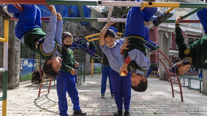 An exile Tibetan child bites into an apple while hanging upside down from iron bars during a break in classes at the Tibetan Children's Village Day School in Dharmsala, India. Thursday, March 24, 2022. The school life is slowly returning to normal after disruptions due to the COVID-19 pandemic. (AP Photo/Ashwini Bhatia)