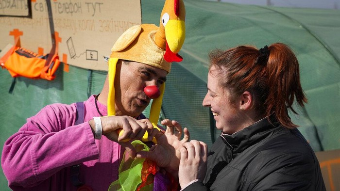 Potret Badut Medis Hibur Anak-anak Pengungsi Ukraina Ukrainian Margarita Zacepina is entertained by Nimrod Eisenberg, a clown from the Dream Doctors organization from Israel, at the border crossing in Medyka, southeastern Poland, on Thursday, March 24, 2022. Medical clowns were in action on Thursday at the Medyka border crossing between Ukraine and Poland to cheer up refugee children and also their parents, and bring a temporary relief from the psychological traumas caused by war and separation. (AP Photo/Sergei Grits)