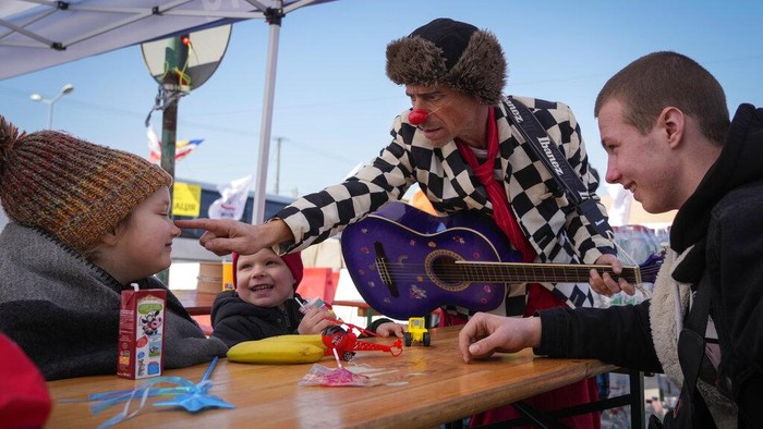 Potret Badut Medis Hibur Anak-anak Pengungsi Ukraina Ukrainian Margarita Zacepina is entertained by Nimrod Eisenberg, a clown from the Dream Doctors organization from Israel, at the border crossing in Medyka, southeastern Poland, on Thursday, March 24, 2022. Medical clowns were in action on Thursday at the Medyka border crossing between Ukraine and Poland to cheer up refugee children and also their parents, and bring a temporary relief from the psychological traumas caused by war and separation. (AP Photo/Sergei Grits)