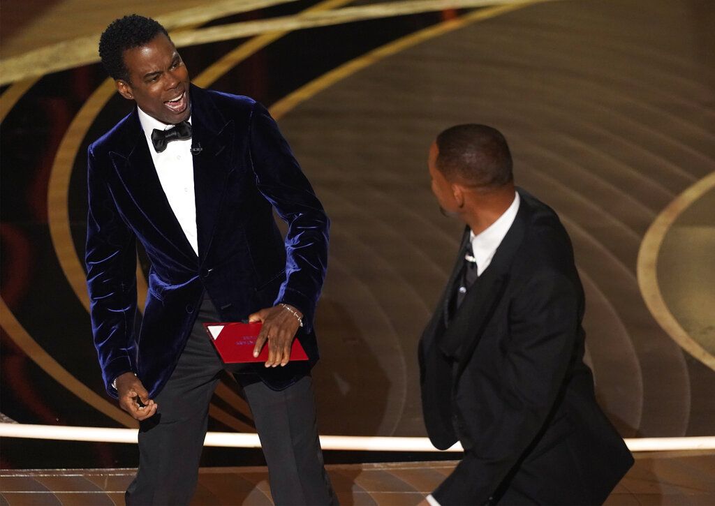 Chris Rock presenter Chris Rock, left, reacts after being hit on stage by Will Smith while presenting the award for best documentary feature at the Oscars on Sunday, March 27, 2022, at the Dolby Theatre in Los Angeles. (AP Photo/Chris Pizzello)
