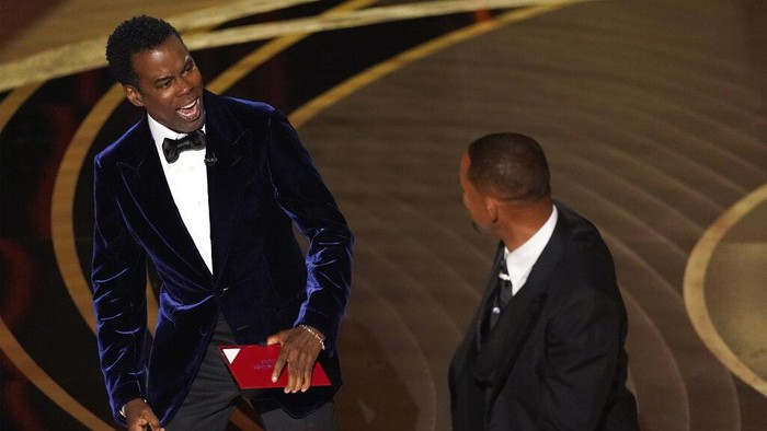 presenter Chris Rock, left, reacts after being hit on stage by Will Smith while presenting the award for best documentary feature at the Oscars on Sunday, March 27, 2022, at the Dolby Theatre in Los Angeles. (AP Photo/Chris Pizzello)