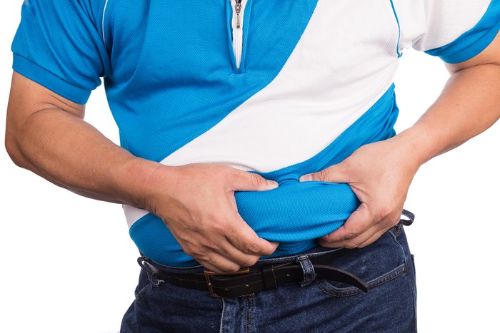Man pinching own unhealthy big belly with visceral or subcutaneous fats. Pose health risk.