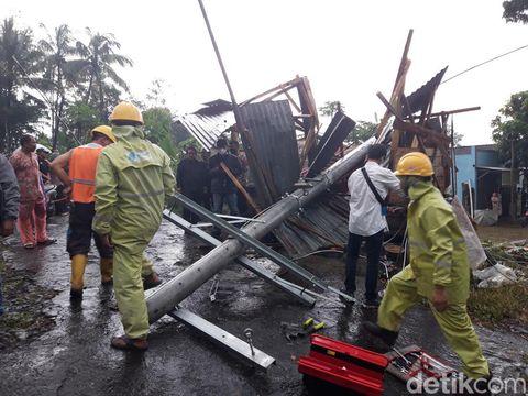 Petugas PLN mengevakuasi tiang listrik yang menimpa warung bakso.