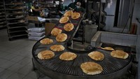 Pekerja toko roti mengemas roti yang baru diproduksi dari jalur produksi di toko roti otomatis di pinggiran selatan Beirut, Dahiyeh, Lebanon. Ukraina dan Rusia merupakan pengekspor utama biji-bijian lain dan minyak biji bunga matahari yang digunakan untuk memasak. (AP/Bilal Husein)
