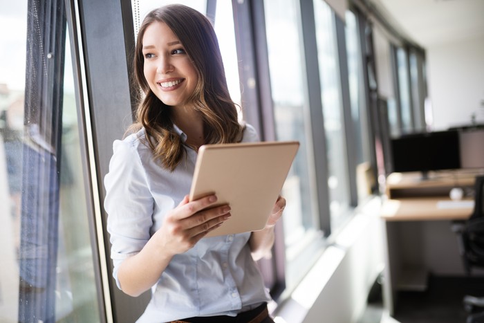 Young businesswoman using a digital tablet while standing in front of windows in office
