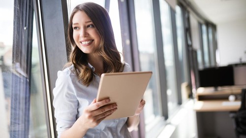 Young businesswoman using a digital tablet while standing in front of windows in office