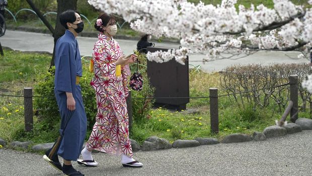 People stop to take pictures as they walk on a sidewalk under a canopy of cherry blossoms Sunday, March 27, 2022, in Tokyo. (AP Photo/Kiichiro Sato)
