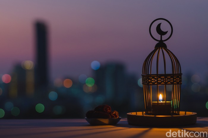 Lantern that have moon symbol on top and small plate of dates fruit with dusk sky and city bokeh light background for the Muslim feast of the holy month of Ramadan Kareem.