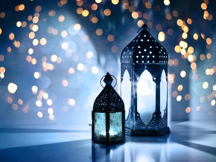 Couple of glowing Moroccan ornamental lanterns on the table. Greeting card, invitation for Muslim holy month Ramadan Kareem, festive blue night background with glittering golden bokeh lights.