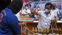 Kabid Indag Direskrimsus Polda Banten Komisaris Candra Sasongko (kanan) melihat tersangka AR (kiri) mengisi botol dengan minyak goreng curah saat rilis kasus pemalsuan minyak goreng curah menjadi minyak goreng kemasan di Serang, Banten, Rabu (30/3/2022).