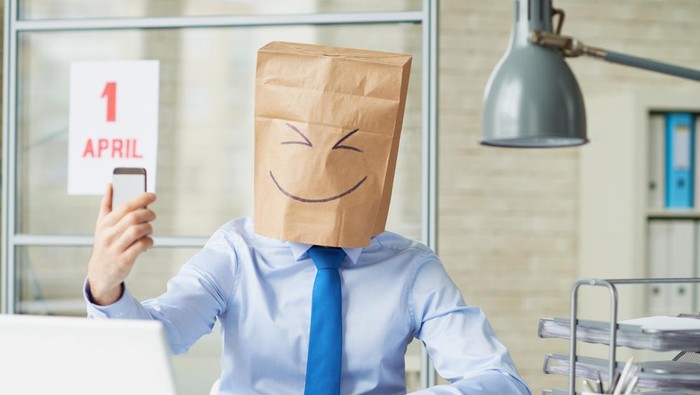 Office worker wearing paper bag taking a selfie with smart phone on April fools day