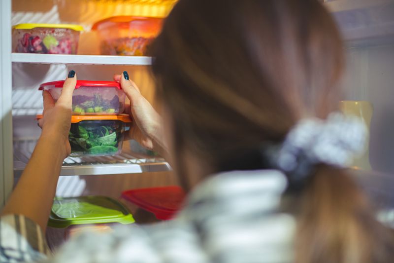 An unrecognizable person is taking out a container filled with chopped veggies from the fridge.