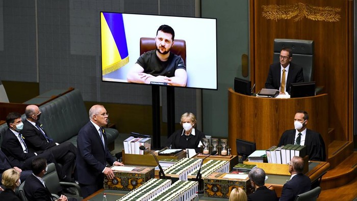 Australian Prime Minister Scott Morrison, standing, welcomes Ukrainian President Volodymyr Zelenskyy to address the House of Representatives via a video link at Parliament House in Canberra, Thursday, March 31, 2022. Zelenskyy appealed directly to Australian lawmakers for more help in its war against Russia including armored vehicles and tougher sanctions. (Lukas Coch/AAP Image via AP)