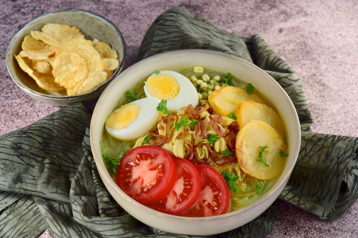 Soto Ayam, yellow turmeric chicken soup with vermicelli noodles, shredded chicken, boiled egg, fried potato, sprouts, tomato, parsley and fried shallots, served with Emping. Popular Indonesian food