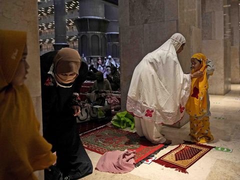 A woman helps her daughter to put on a praying robe prior to the start of 'tarawih' an evening prayer marking the first eve of the holy fasting month of Ramadan at Istiqlal Mosque in Jakarta, Indonesia, Saturday, April 2, 2022. (AP Photo/Dita Alangkara)