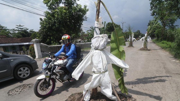 PROTES JALAN RUSAK DI KEDIRI Pengendara sepeda motor melintas di jalan rusak yang ditanami tanaman pisang dan tebu di Desa Janti, Kediri, Jawa Timur, Sabtu (2/4/2022). Warga daerah setempat memberi tanda pada lubang jalan dengan menanam tanaman tebu dan pisang sekaligus memasang baju alat pelindung diri (APD) bekas sebagai bentuk protes karena jalan rusak yang tidak kunjung diperbaiki. ANTARA FOTO/Prasetia Fauzani/foc.