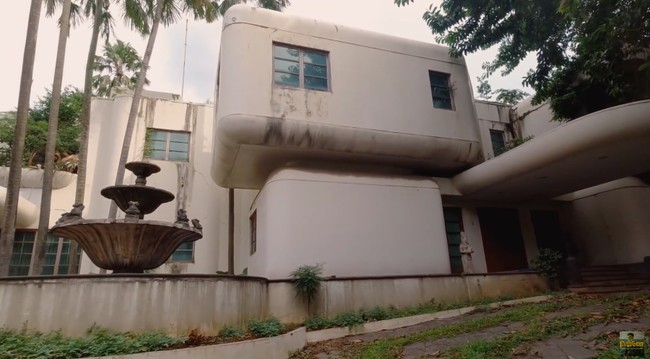 YouTuber bernama Papi Story mendokumentasikan kunjungannya ke sebuah rumah mewah yang sudah tak bertuan. Tampak depan, rumah tersebut seperti bangunan berarsitekur futuristik 90-an yang unik karena penuh lekukan pada sudut-sudutnya. (Foto: YouTube/Papi Story)