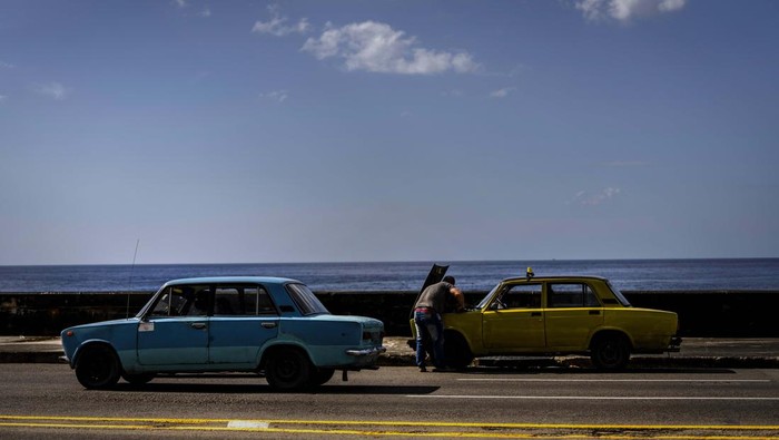Rusia Serang Ukraina, Mobil-mobil Tua di Kuba Terancam Rusak A man tries to repair his vintage Russian-made Lada car at the Malecon, in Havana, Cuba, Friday, April 1, 2022. Global restrictions on transport and trade with Russia after its invasion of Ukraine pose a serious problem for Cubans because much of the island's fleets of trucks, buses, cars and tractors came from distant Russia and are now aging and in need of parts. (AP Photo/Ramon Espinosa)
