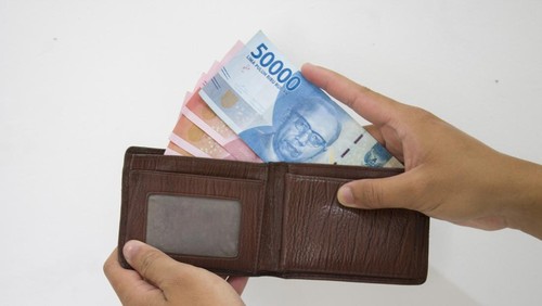 Hand holding Indonesian Rupiah (IDR) Red 100,000 bank notes currency from leather wallet on white background.