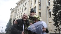 Pasangan Anastasia dan Anton memeluk seorang prajurit Ukraina di tengah upacara pernikahan yang digelar di Kharkiv pada akhir pekan lalu.  