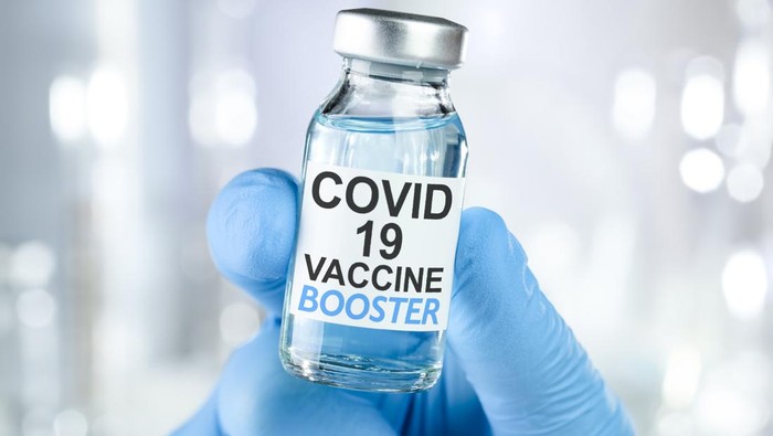 Hand in blue medical gloves holding a vaccine vial with Covid 19 Vaccine Booster text, for Coronavirus booster shot.