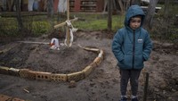Di halaman rumahnya, Vlad Tanyuk (6), berdiri di dekat makam ibunya Ira Tanyuk, yang meninggal karena kelaparan dan stres akibat perang, di pinggiran Kyiv, Ukraina, Senin, (4/4/2022). (AP Photo/Rodrigo Abd)