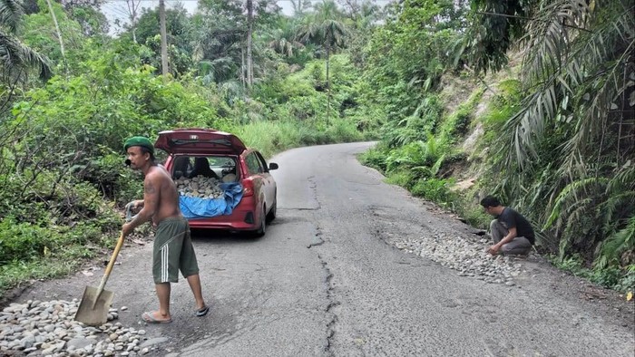 Dua warga menimbun jalan rusak