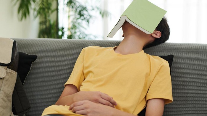Teenage boy fell asleep on sofa in living room with opened book on his face