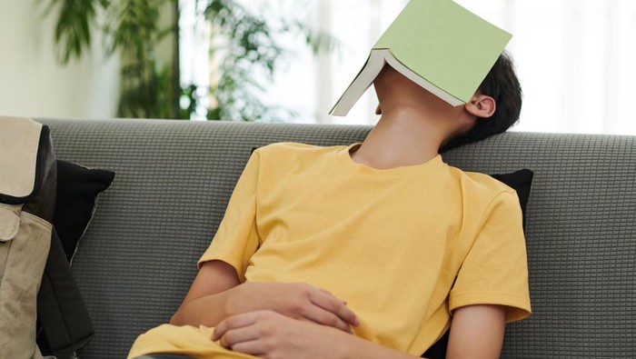 Mimpi basah bikin batal puasa? Teenage boy fell asleep on sofa in living room with opened book on his face