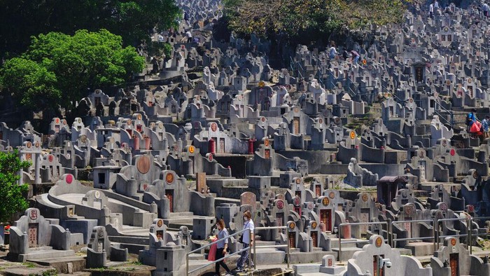 Potret Tradisi Menghormati Leluhur dan Kerabat di Hong Kong A man wearing face mask burns paper money at the gravesite of a relative in a cemetery during the Chinese Ching Ming, or Tomb Sweeping Day, in Hong Kong Tuesday, April 5, 2022. Thousands of Hong Kong residents pay respects to their ancestors and relatives during the annual festival. (AP Photo/Vincent Yu)