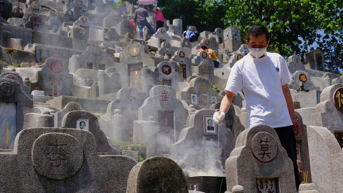 Potret Tradisi Menghormati Leluhur dan Kerabat di Hong Kong A man wearing face mask burns paper money at the gravesite of a relative in a cemetery during the Chinese Ching Ming, or Tomb Sweeping Day, in Hong Kong Tuesday, April 5, 2022. Thousands of Hong Kong residents pay respects to their ancestors and relatives during the annual festival. (AP Photo/Vincent Yu)