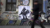 Warga melintas di depan mural yang menggambarkan Presiden Vladimir Putin menggotong mayatnya sendiri, di Sofia, Bulgaria beberapa waktu lalu. Mural ini karya seniman Bulgaria, Stanislav Beloski.