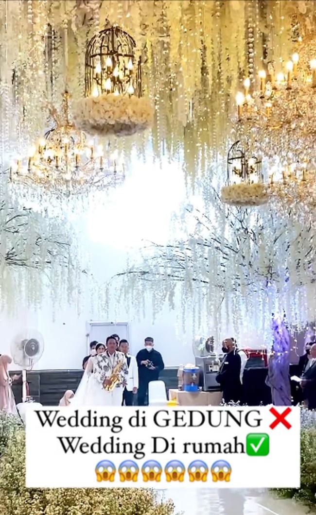 Pasangan pengantin yang viral itu menyulap rumah jadi bak hotel mewah. Area rumah dipasang tenda putih dan didekorasi dengan tema rustic modern. Lokasi acara pernikahan terlihat luas dan bikin takjub. Terlihat pengantin berjalan ke pelaminan diiringi oleh keluarga dan pemain saxophone.  Foto: Dok. @_cocoentertainment.